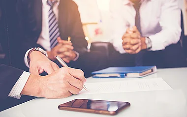 Geschäftstreffen: Eine Hand hält einen Stift über Dokumente auf dem Tisch.
