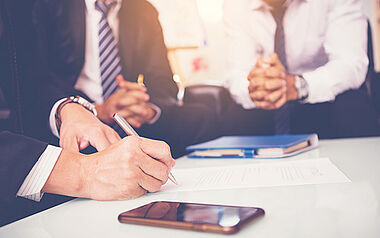 Geschäftstreffen: Eine Hand hält einen Stift über Dokumente auf dem Tisch.