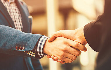 Ein Handschlag zwischen Geschäftspartnern im Bürokontext.