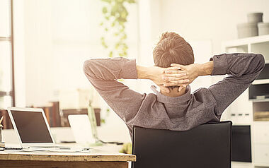 Ein Mann sitzt am Schreibtisch und blickt nachdenklich in die Ferne.